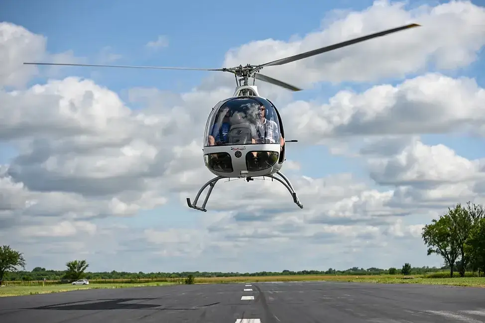 Front view of helicopter flying over runway with two pilot in the cockpit